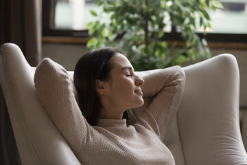 Relaxed calm positive millennial girl resting in comfortable armchair, leaning back with sleepy...
