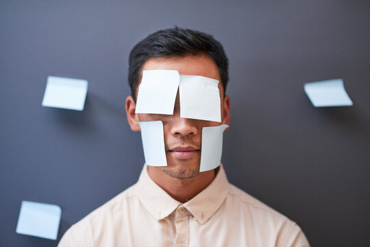 An Asian businessman stands with sticky notes on his face looking tired at work - Powered by Adobe