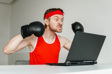 Funny angry sportsman geek wearing boxing gloves using laptop.