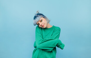 Hipster girl with blue hair and in a green sweatshirt posing for the camera on a blue background