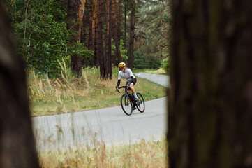 Naklejka premium A sporty man in cycling gear trains outside the city on a bicycle in the middle of the forest.