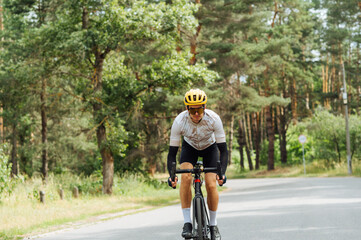 Athletic young man in outfit rides a bicycle in the summer outside the city in the woods on an asphalt road.