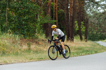 Handsome athletic man on a bicycle walks outside the city in the woods on an asphalt road.