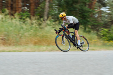 A professional cyclist in sportswear rides quickly on a country road.