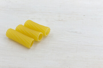 Uncooked short pasta tubes, elicoidali on a wooden white table, closeup