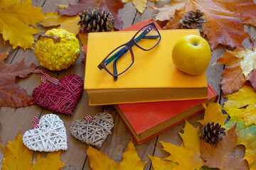 Autumn background. Old books, apple, glasses and decorative hearts on wooden planks with autumn leaves. Autumn design concept.