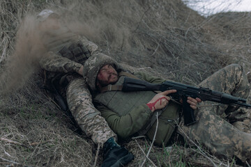 Two Ukrainian soldiers lie with kalashnikov assault rifles on dry grass during artillery...