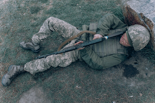 Ukrainian wounded soldier lying down on grass near rock after battle against russian enemy.