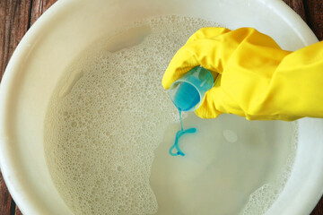 Female hands holding a wash basin with water and washing liquid flat lay background. Hand wash concept. Woman pouring a detergent in a water.