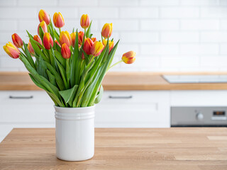 A beautiful bouquet of red and yellow tulips in a white vase on a wooden countertop against a white kitchen background. Spring time concept. Copy space