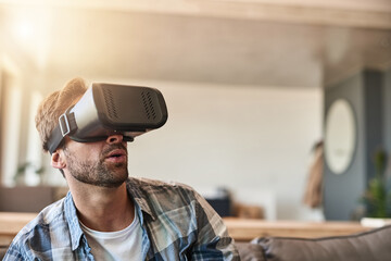 Dont just watch a movie, experience it. Shot of a young man using a virtual reality headset on the sofa at home.