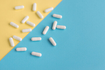 White pills on a yellow and blue pastel background. Capsules pills close-up. health care and medicine.
