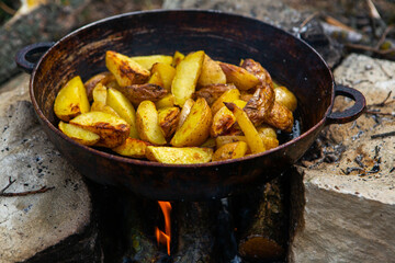 Homemade crispy potatoes on a frying pan on the fire outside. Picnic in nature with cooking.