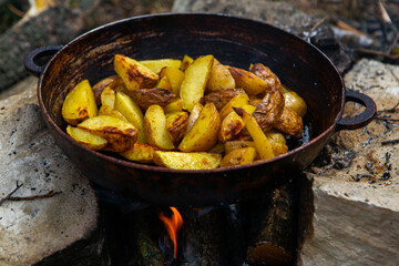 Homemade crispy potatoes on a frying pan on the fire outside. Picnic in nature with cooking.