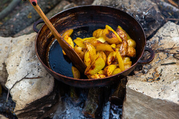 Homemade crispy potatoes on a frying pan on the fire outside. Picnic in nature with cooking.