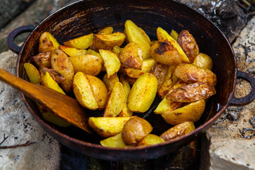 Homemade crispy potatoes on a frying pan on the fire outside. Picnic in nature with cooking.