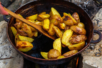 Homemade crispy potatoes on a frying pan on the fire outside. Picnic in nature with cooking.