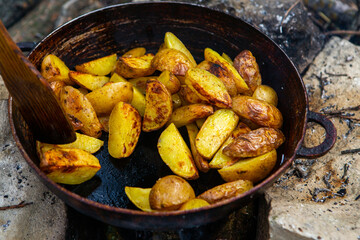 Homemade crispy potatoes on a frying pan on the fire outside. Picnic in nature with cooking.