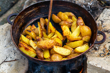 Homemade crispy potatoes on a frying pan on the fire outside. Picnic in nature with cooking.