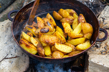 Homemade crispy potatoes on a frying pan on the fire outside. Picnic in nature with cooking.