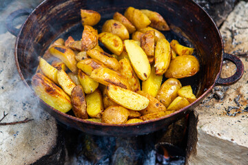 Homemade crispy potatoes on a frying pan on the fire outside. Picnic in nature with cooking.