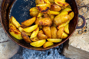 Homemade crispy potatoes on a frying pan on the fire outside. Picnic in nature with cooking.