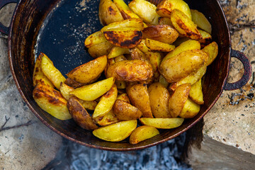 Homemade crispy potatoes on a frying pan on the fire outside. Picnic in nature with cooking.
