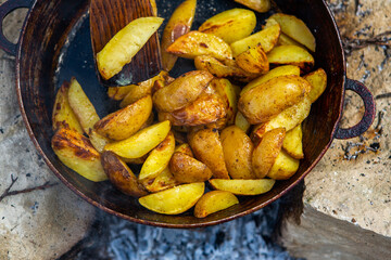Homemade crispy potatoes on a frying pan on the fire outside. Picnic in nature with cooking.