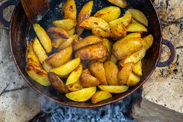 Homemade crispy potatoes on a frying pan on the fire outside. Picnic in nature with cooking.