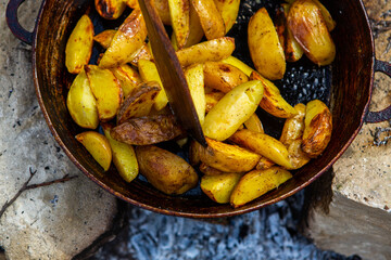 Homemade crispy potatoes on a frying pan on the fire outside. Picnic in nature with cooking.