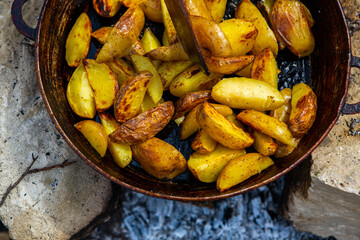 Homemade crispy potatoes on a frying pan on the fire outside. Picnic in nature with cooking.