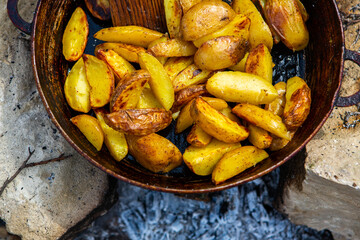Homemade crispy potatoes on a frying pan on the fire outside. Picnic in nature with cooking.