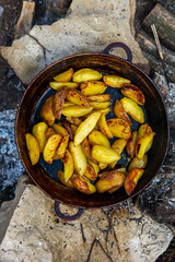 Homemade crispy potatoes on a frying pan on the fire outside. Picnic in nature with cooking.