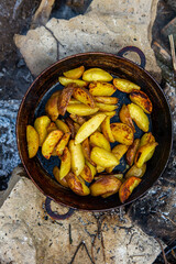 Homemade crispy potatoes on a frying pan on the fire outside. Picnic in nature with cooking.