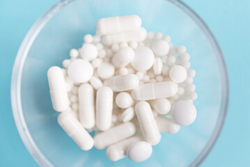Different white pills and a plastic container on a blue background. Medical theme.