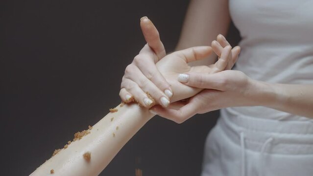 Woman enjoying a sugar sea salt natural body scrub exfoliation treatment with professional beautician. Action. Concept of beauty and body care.