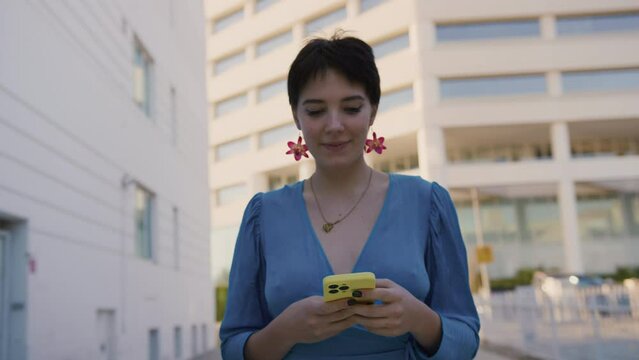 Attractive cheerful girl in blue romantic dress on weekend, travel smiling, walking on the street with mobile phone in hands. Romantic blogger girl chatting, planning, scrolling through social media