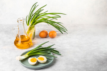 Fresh green onions, boiled eggs and vegetable oil on a light background. Simple and healthy breakfast. Copy space