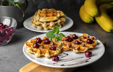 Belgian or Brussels waffles with frozen cherries. Homemade cottage cheese banana waffle in a plate on a dark table
