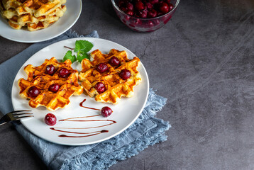 Belgian or Brussels waffles with frozen cherries. Homemade cottage cheese banana waffle in a plate on a dark table. Copy space