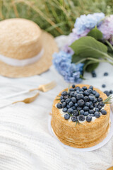 Cake with blueberries blue hydrangea and a hat on a summer picnic