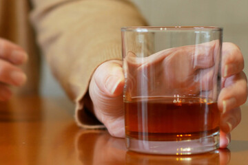 shaking woman hand reaching of glass with whiskey standing on a wooden table, woman's alcoholism problem