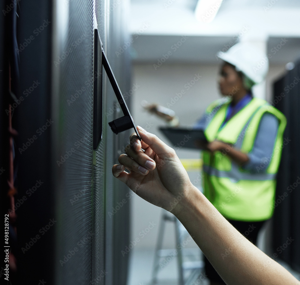 Poster Time to open up this panel. Closeup shot of an unrecognizable female programmer working in a server room with a colleague in the background.
