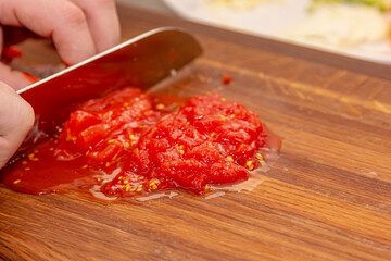The cook cuts the pulp of a tomato with a knife on a wooden board