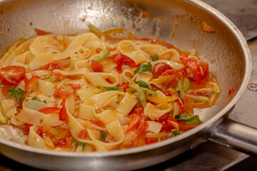 The chef prepares Pappardelle or Linguini pasta in tomato sauce in a steel pan.
