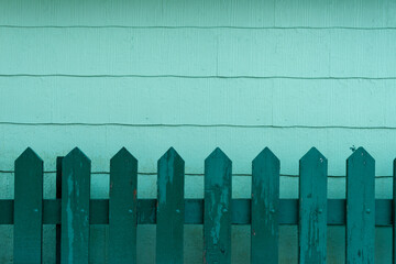 A vintage green wooden picket fence made of rough boards. The rustic fence is in front of a...