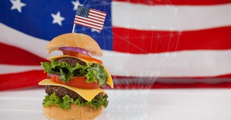 Miniature american flag over a burger on wooden surface against american flag in background
