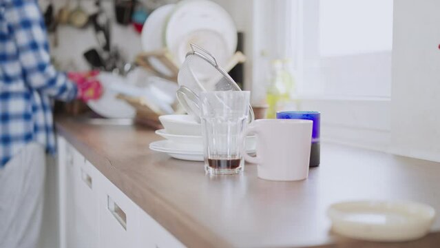 hand washing the dishes concept on the background defocus woman standing near kitchen sink on the foreground dirty dishes