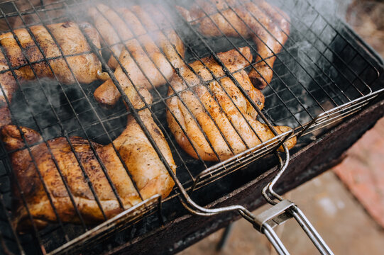 Chicken thighs are fried on the grill in a barbecue with smoke in nature.