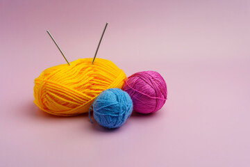 Yarn for knitting different colors on a pink background. The spokes are stuck in